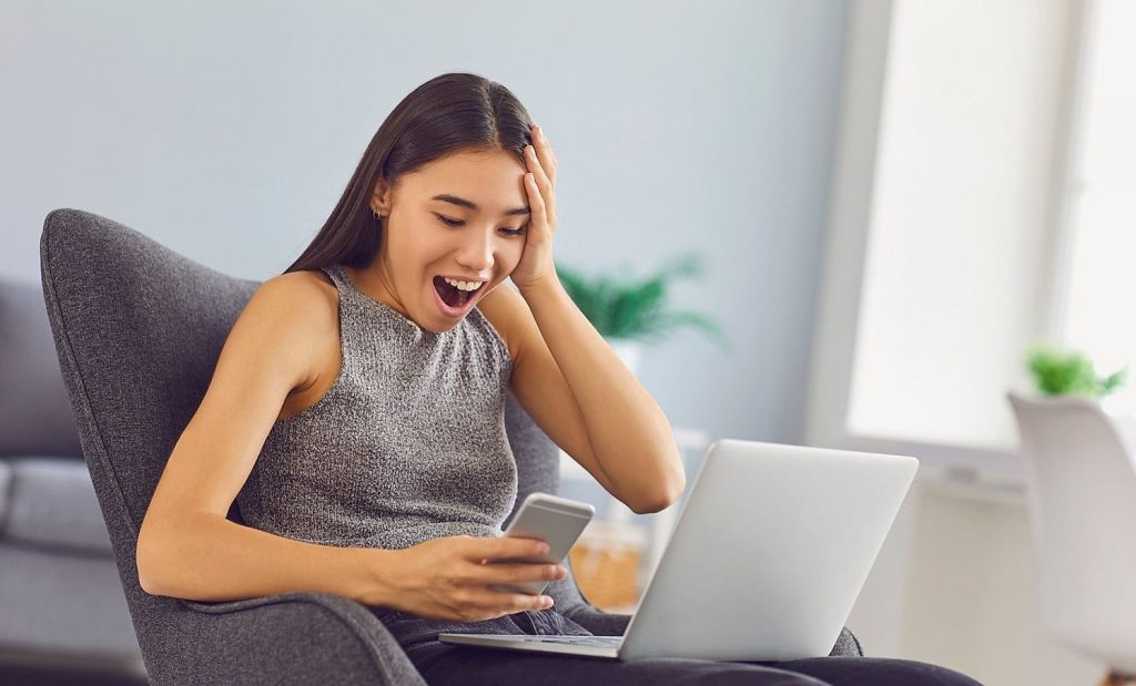Happy young girl playing on smartphone, sitting in armchair at home